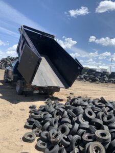 A Hagen's Junk Removal truck dumping a large pile of old tires at a recycling facility in Fort Collins, CO.