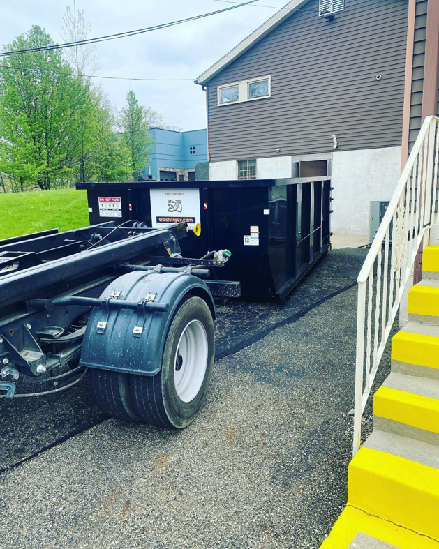A trash_tiger truck delivering or picking up a dumpster for junk removal services next to a commercial building in Canton, OH.