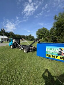 A Barkers Junk Removal & Hauling LLC truck with a blue roll-off dumpster for rental on a grassy area in Roanoke, VA.