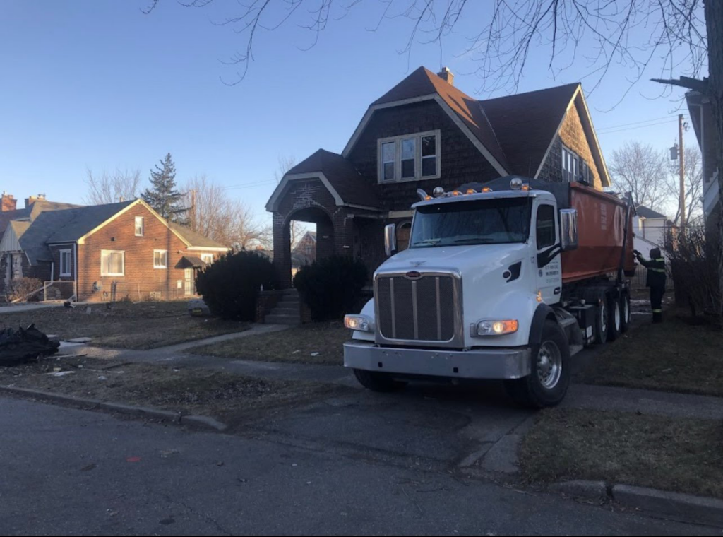 A Century Waste Management truck with a roll-off dumpster at a residential property for junk removal in Sterling Heights, MI.