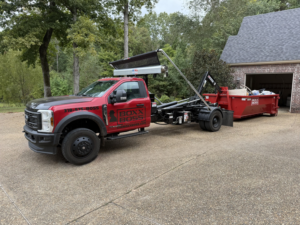 A Boxx Boss Solutions junk removal truck with a filled dumpster on a residential driveway in Bossier City, LA.
