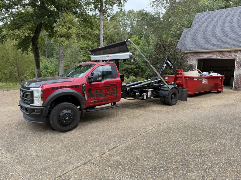 A Boxx Boss Solutions junk removal truck with a filled dumpster on a residential driveway in Bossier City, LA.