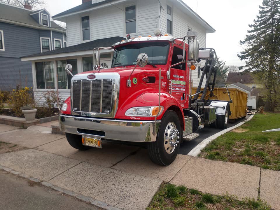 A red junk removal truck and yellow dumpster from Champion Waste Removal, Inc. parked at a residential property in Orange, NJ.