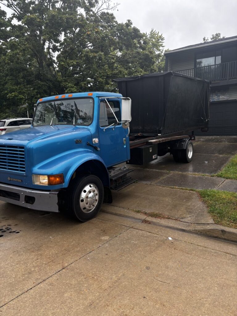 A blue roll-off truck with a black dumpster on its bed, ready for general junk removal services by Wagners Property Services LLC in Canton, OH.