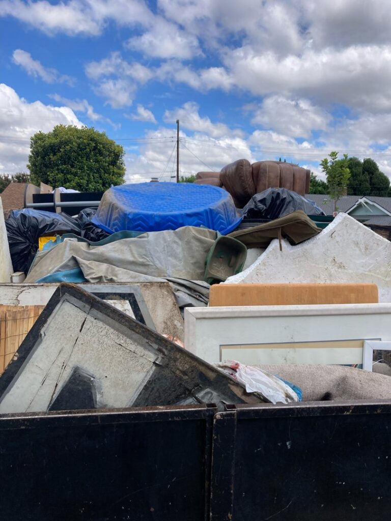 A junk removal truck completely full of various debris, including a blue kiddie pool, ready for disposal by Larry The Rubbish Man in Los Angeles, CA.