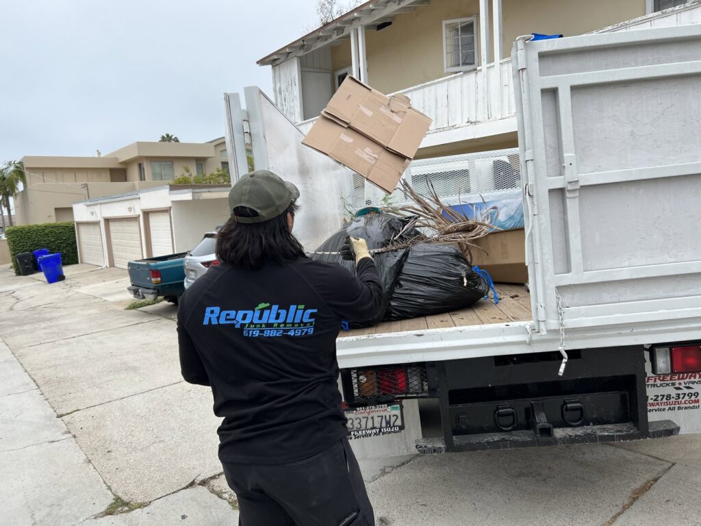 A Republic Junk Removal truck filled with various debris and junk, with a worker standing nearby in San Diego, CA.