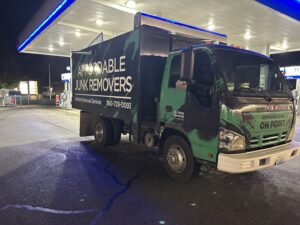 An OnPoint Removal Services truck, branded 'Affordable Junk Removers', parked at a gas station at night in Vancouver, WA.