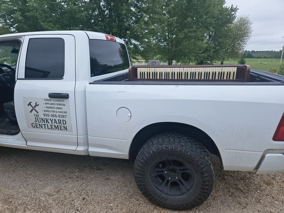A branded junk removal truck from The Junkyard Gentlemen LLC hauling an old organ in Appleton, WI.
