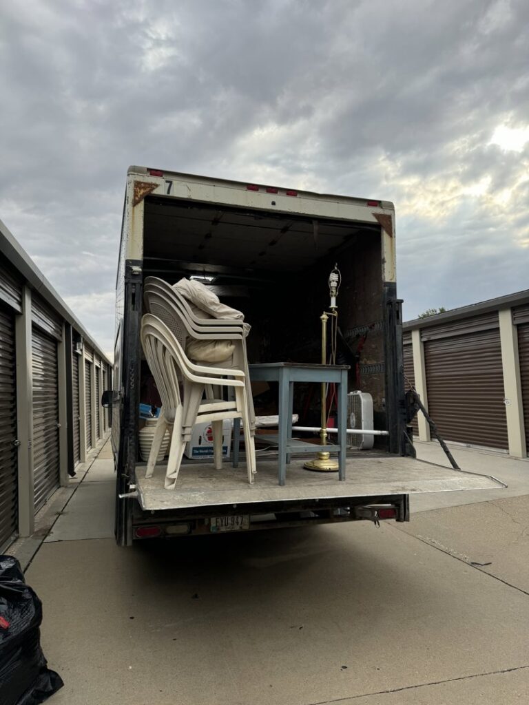 A Kaveman Hauling LLC truck with its ramp down, loaded with furniture and other items for junk removal in Ankeny, IA.
