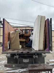 A junk removal truck from 402 Junk Removal in Lincoln, NE, loaded with a mattress, chairs, and various debris, ready for hauling.