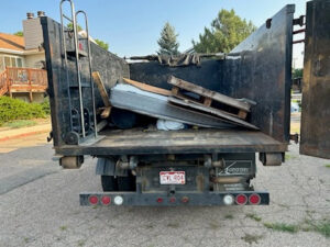 The back of a Hagen's Junk Removal truck loaded with a mattress, wooden pallets, and other debris in Fort Collins, CO.