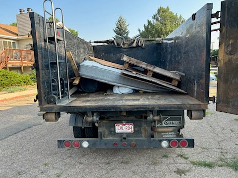 The back of a Hagen's Junk Removal truck loaded with a mattress, wooden pallets, and other debris in Fort Collins, CO.