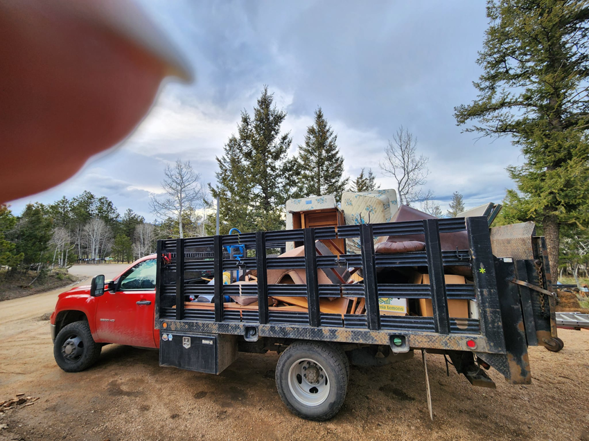 A red junk removal truck loaded with furniture and other items by Bear Foot Junk Removal in Bailey, CO.