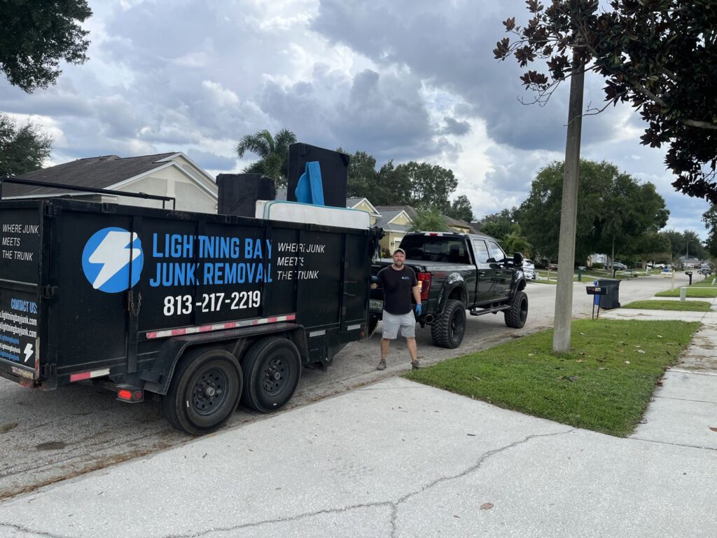 A Lightning Bay Junk Removal truck and trailer loaded with furniture and a mattress, ready for transport in Tampa, FL.