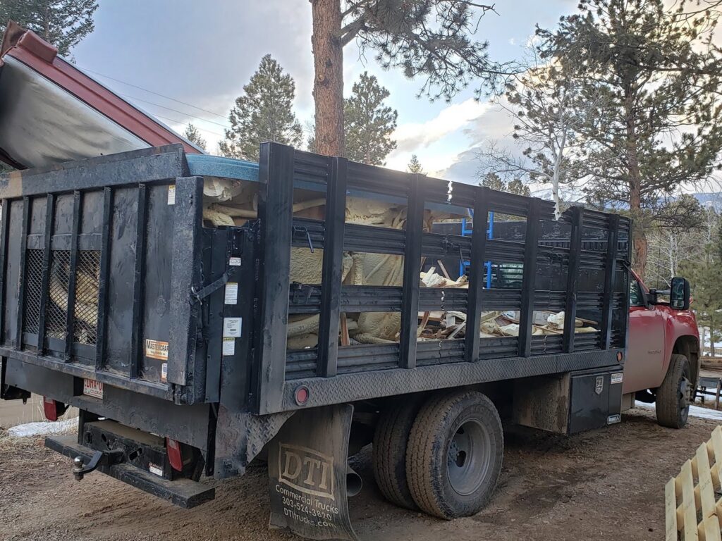 A red junk removal truck loaded with insulation and construction debris by Bear Foot Junk Removal in Bailey, CO.