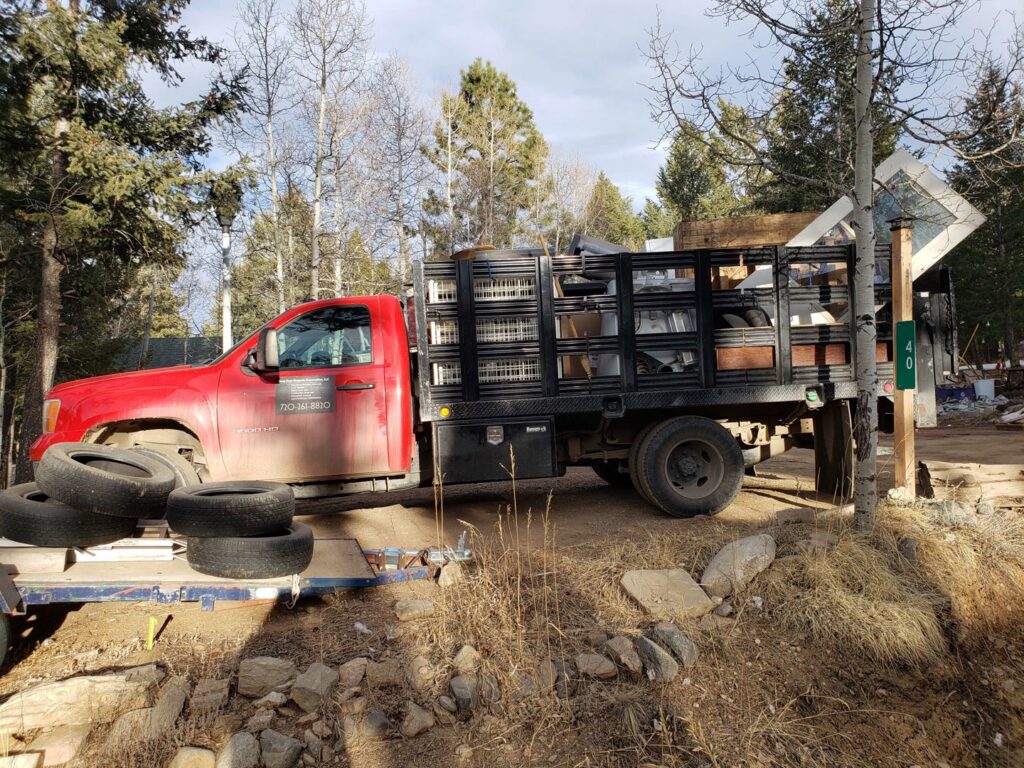 A red junk removal truck loaded with tires, windows, and other debris by Bear Foot Junk Removal in Bailey, CO.