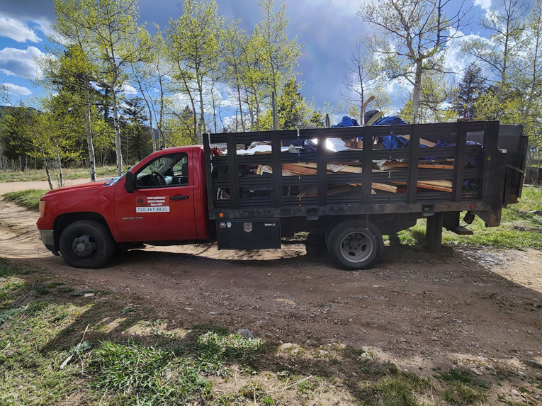 A red junk removal truck loaded with wood debris and tarps by Bear Foot Junk Removal in Bailey, CO.