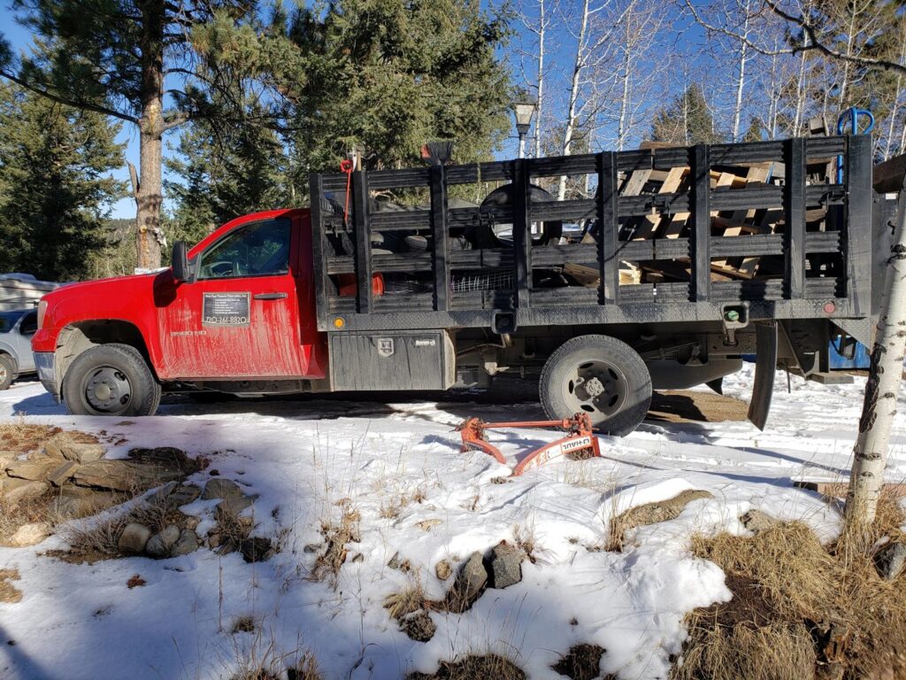 A red junk removal truck loaded with wood debris in a snowy setting by Bear Foot Junk Removal in Bailey, CO.