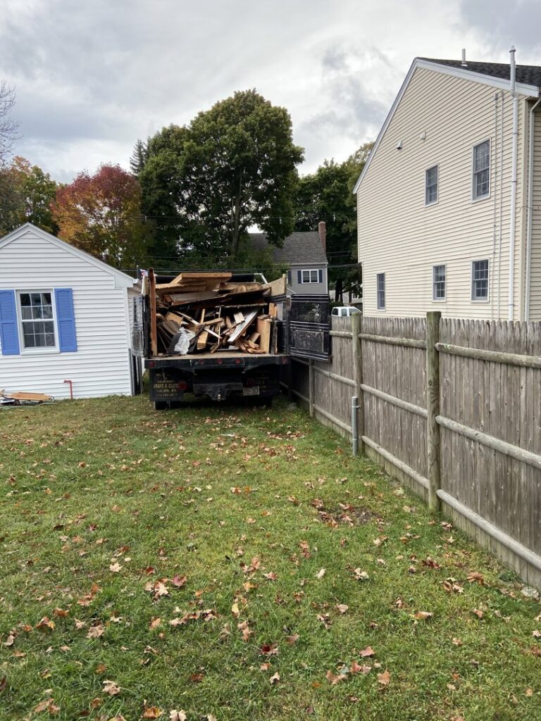 A junk removal truck loaded with wood and construction debris in a backyard in Lynn, MA by Altri Junk Removal Services.