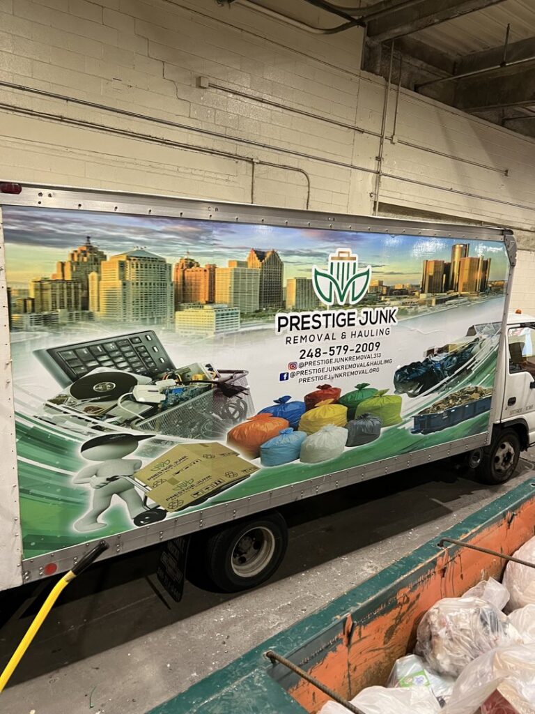 A Prestige Junk Removal & Hauling truck backed up to a loading dock, with bags of trash visible, demonstrating active junk removal in Detroit, MI.
