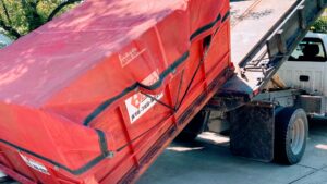 A junk removal truck loading a red tarped dumpster for AA Quick Disposal in Kansas City, MO.