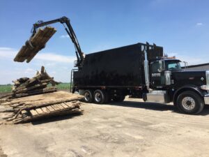A Blackwood Solutions INC junk removal truck loading old wooden debris with a grapple arm in Bloomington, IN.