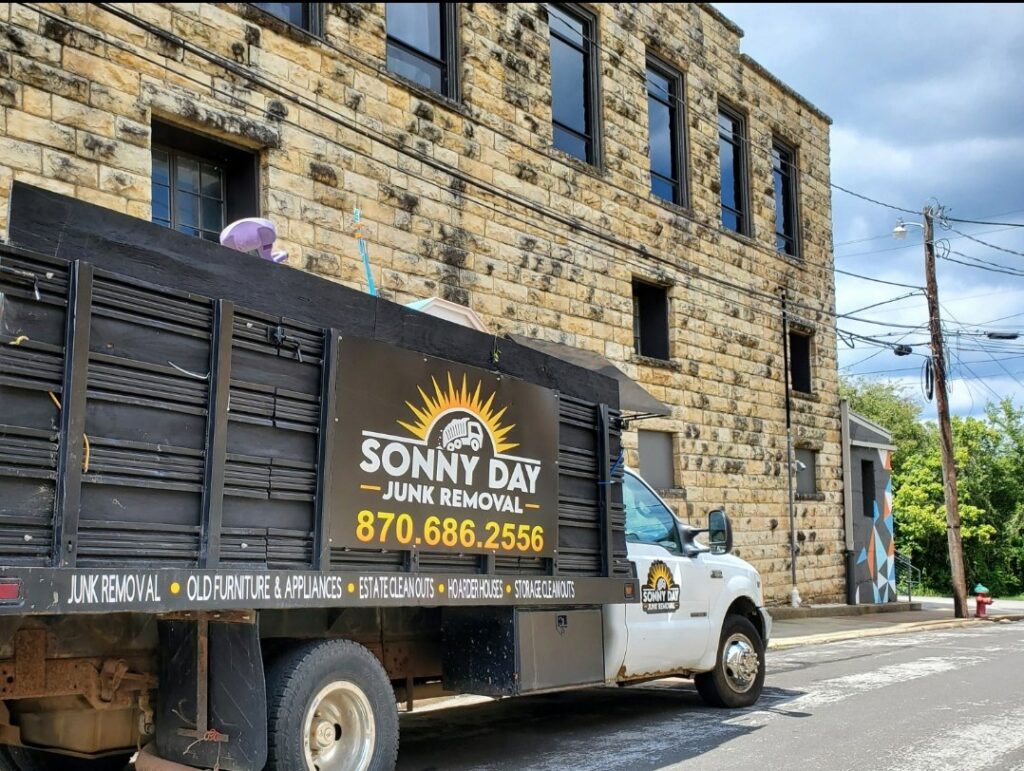 A Sonny Day Junk Removal truck parked on a street next to a stone building, ready for a job in Batesville, AR.