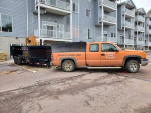 A BeeBop's Junk Removal truck and trailer parked outside an apartment complex in Sioux Falls, SD.