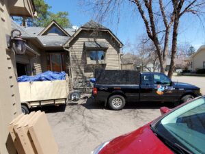 A BeeBop's Junk Removal truck pulling a tarp-covered trailer in a residential driveway in Sioux Falls, SD.