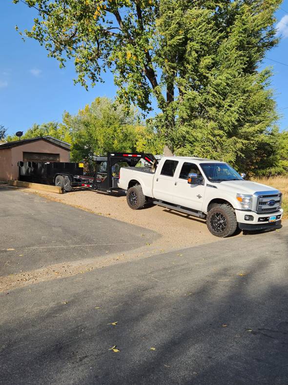 A white Ford truck with a dump trailer parked on a residential driveway, ready for junk removal by Outlaw Rental in Bismarck, ND.
