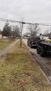A 614junkremoval truck towing a loaded trailer with junk covered by a tarp on a residential street in Columbus, OH.