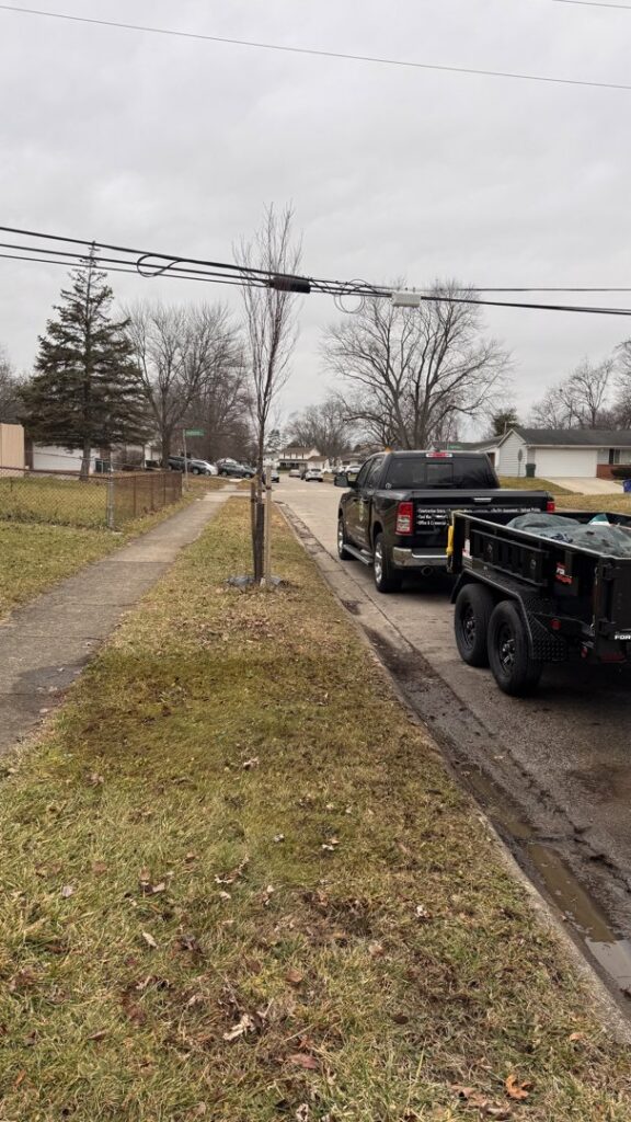 A 614junkremoval truck towing a loaded trailer with junk covered by a tarp on a residential street in Columbus, OH.