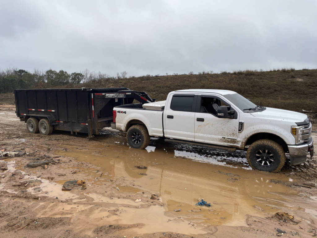 A Merritt Hauling and Disposal truck with a dump trailer parked on a muddy job site for junk removal in Columbus, GA.