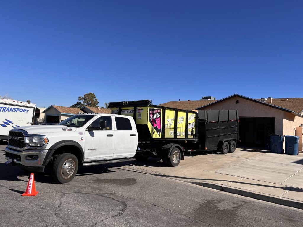 A junk removal truck and trailer with a branded dumpster at a residential job site for Las Vegas Hauling Junk & Moving in Las Vegas, NV