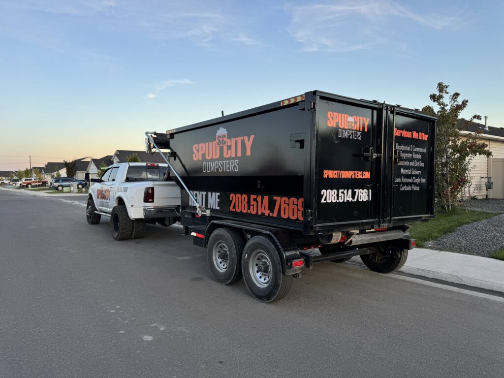 A SpudCity Dumpsters truck pulling a junk removal dumpster trailer on a street in Caldwell, ID.