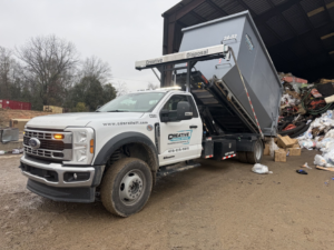 A Creative Disposal Services truck unloading a dumpster full of general junk and debris at a disposal site in Macon, GA.