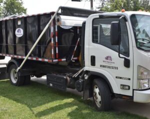 A white junk removal truck with a black roll-off dumpster from Wint Services, LLC, parked on a lawn in Colorado Springs, CO.