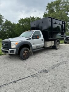 A silver Ford truck equipped with a black junk removal container, branded for Junk It OR Dump It in Independence, MO.