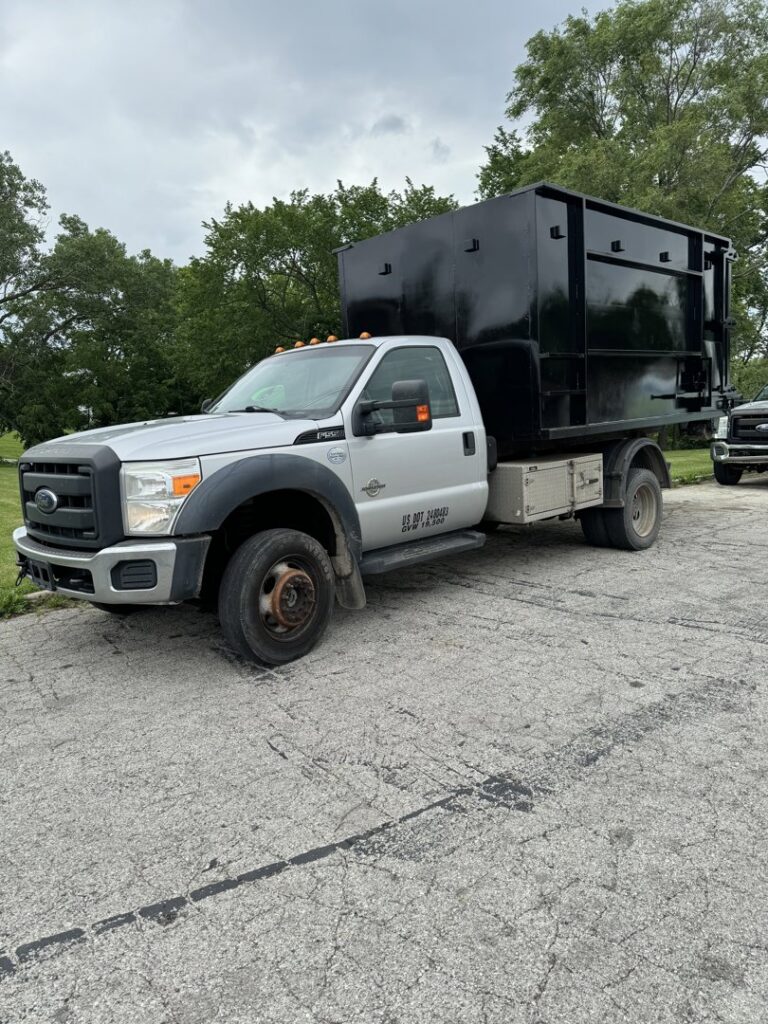 A silver Ford truck equipped with a black junk removal container, branded for Junk It OR Dump It in Independence, MO.