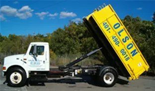 A Greg Olson Trucking junk removal truck with an empty yellow dumpster in East Providence, RI.