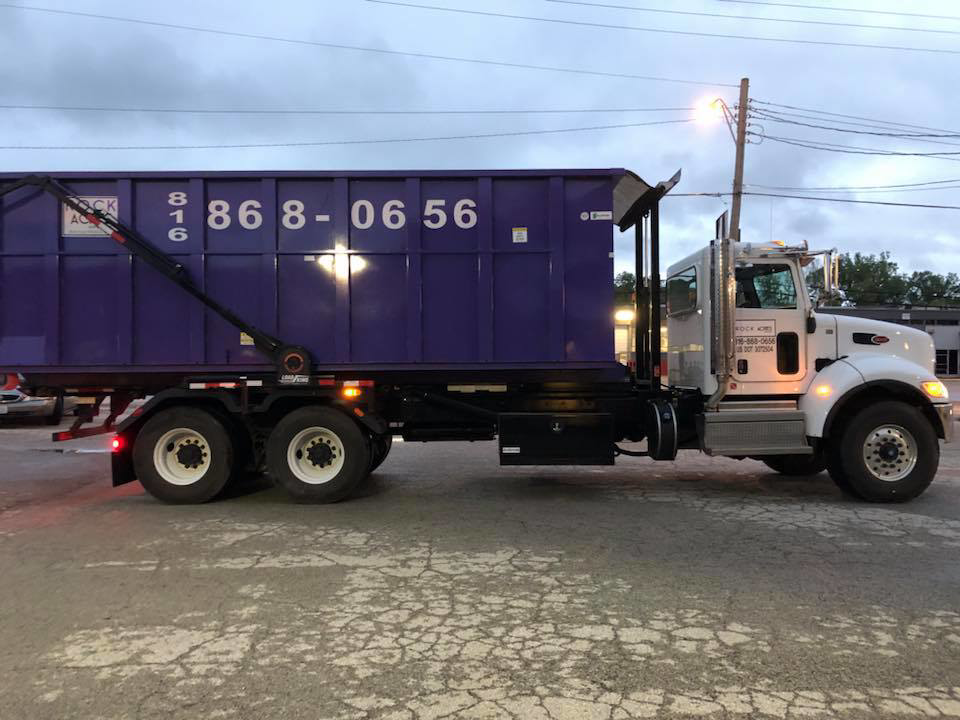 A Rock Acres Companies junk removal truck with a purple roll-off dumpster in Kansas City, MO.