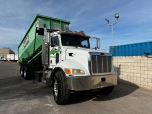 A white Peterbilt truck with a green dumpster on its back, ready for junk removal services from Junk Control in Henderson, NV.