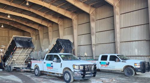 Two GoGo Junk Removal trucks and trailers dumping debris inside a large warehouse in Atlanta, GA.