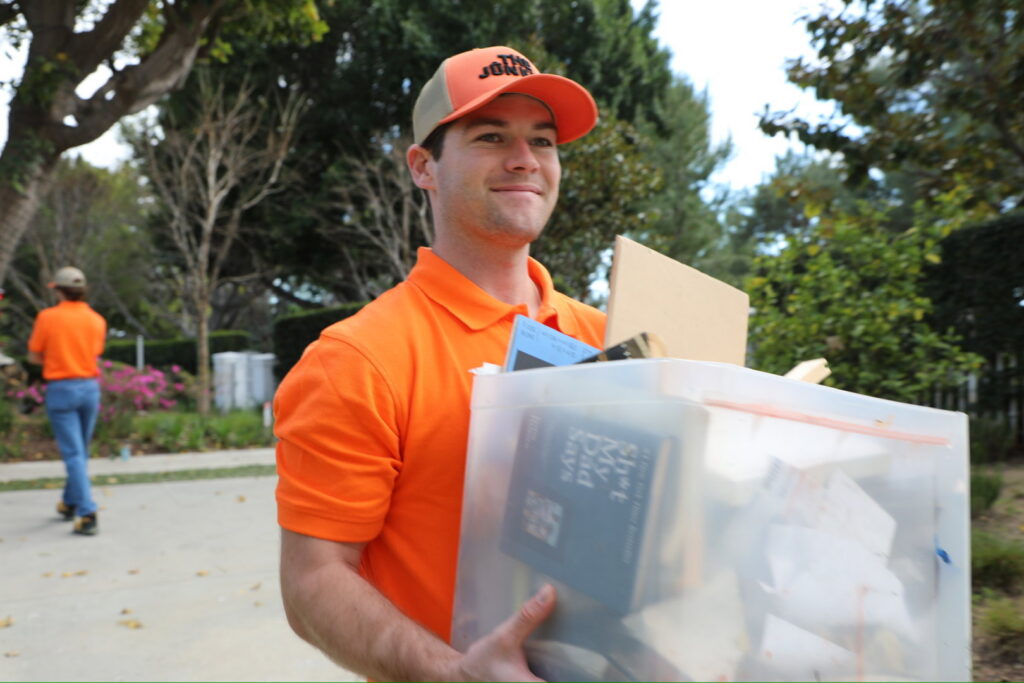 A The Junkiez Junk Removal worker carrying a clear bin filled with various items for disposal in Los Angeles, CA.