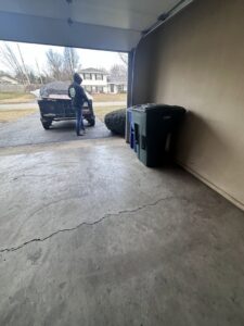 A 614junkremoval worker standing by a loaded junk removal trailer covered with a tarp, viewed from inside a garage in Columbus, OH.