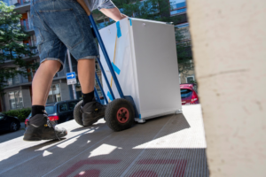 A Junk It OR Dump It worker in Independence, MO, moving a large appliance onto a truck using a hand truck.