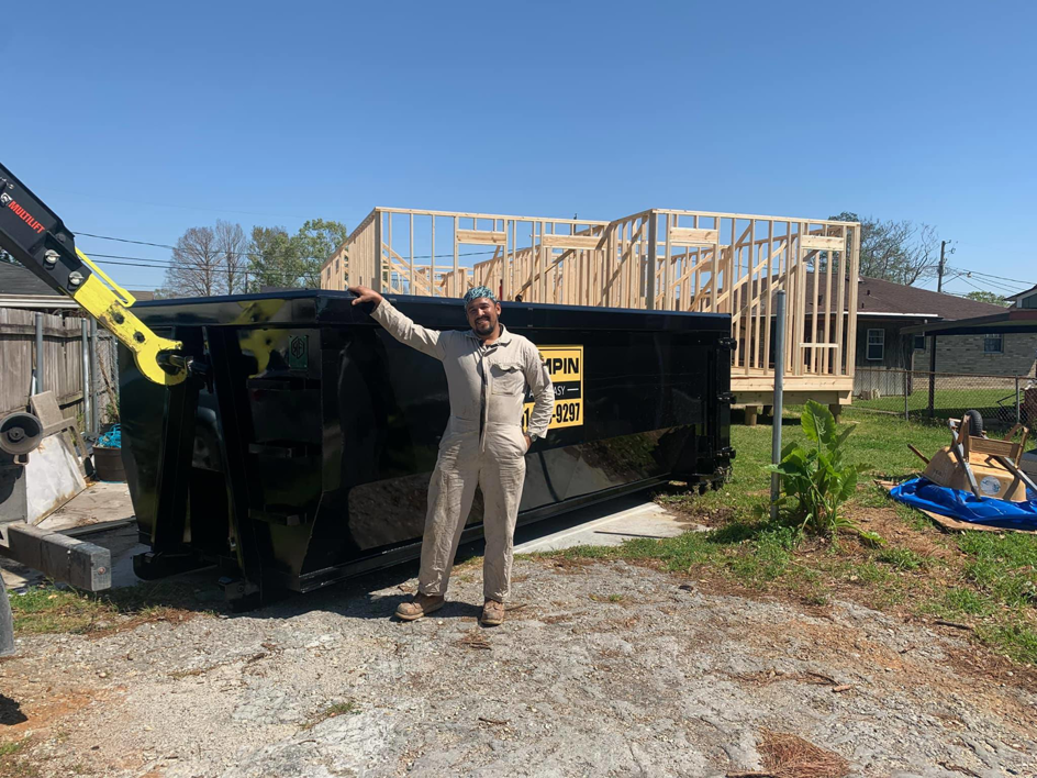 A Dumpin Ain't Easy worker standing next to a large branded dumpster at a construction site in Westwego, LA.