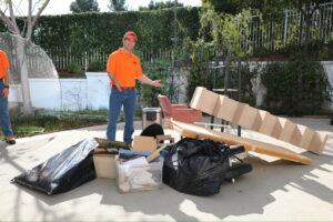 A The Junkiez Junk Removal worker standing next to a pile of collected junk and debris on a patio in Los Angeles, CA.