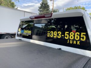 The back window of a Junk Solutions pickup truck displaying the business logo and phone number in Ogden, UT.