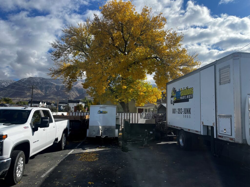 Junk Solutions' white pickup truck, large box truck, and trailers parked in a lot in Ogden, UT, ready for service.